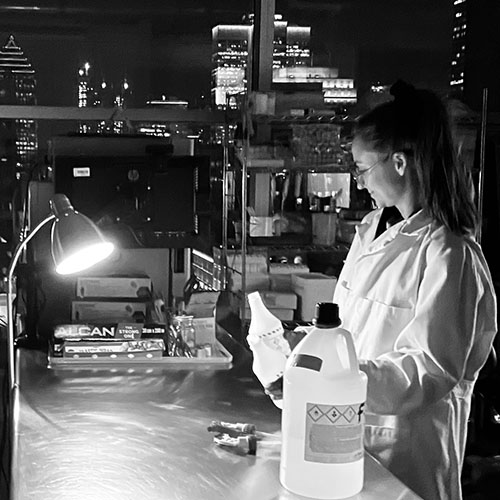 Alexandra Bachmayer works in the Milieux 'Speculative Life' BioLab after dark, seen in her lab coat at the bench in black and white.